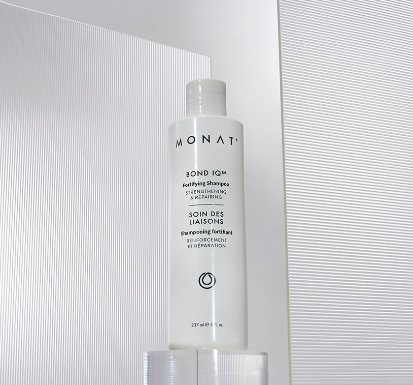 MONAT Bond IQ™ Fortifying Shampoo bottle standing upright on a clear acrylic stand against a textured white, ridged background