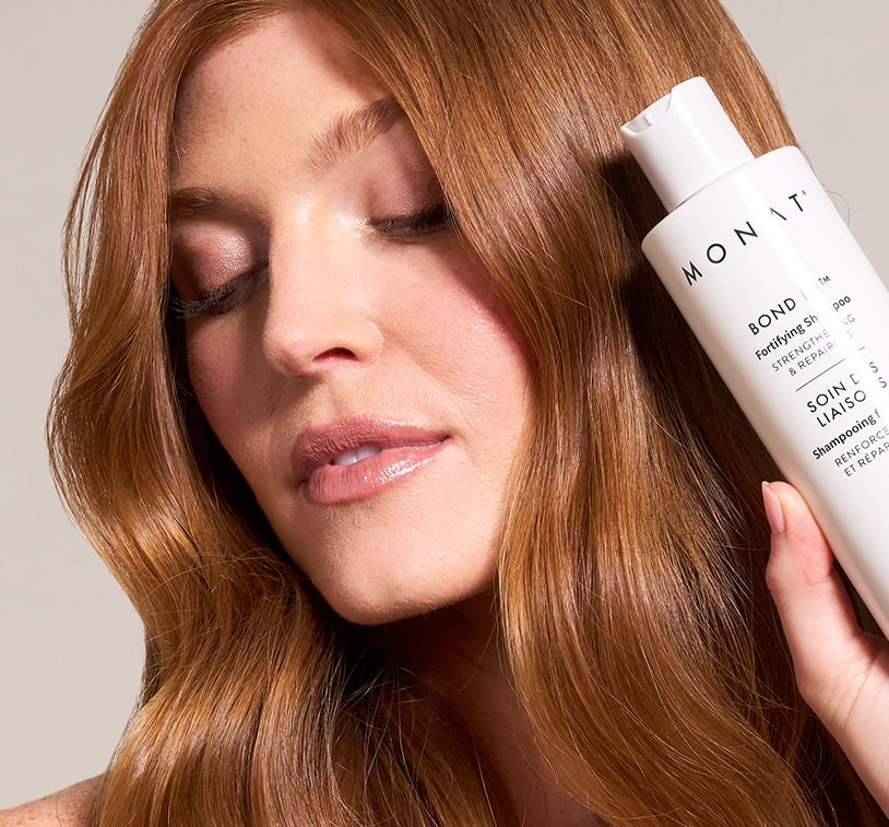 Close-up of a woman with healthy, voluminous hair, smiling while holding the shampoo bottle