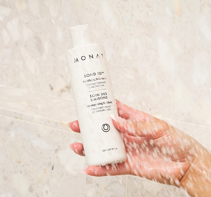 MONAT BOND IQ™ Fortifying Shampoo bottle held upright in front of a light beige marble surface