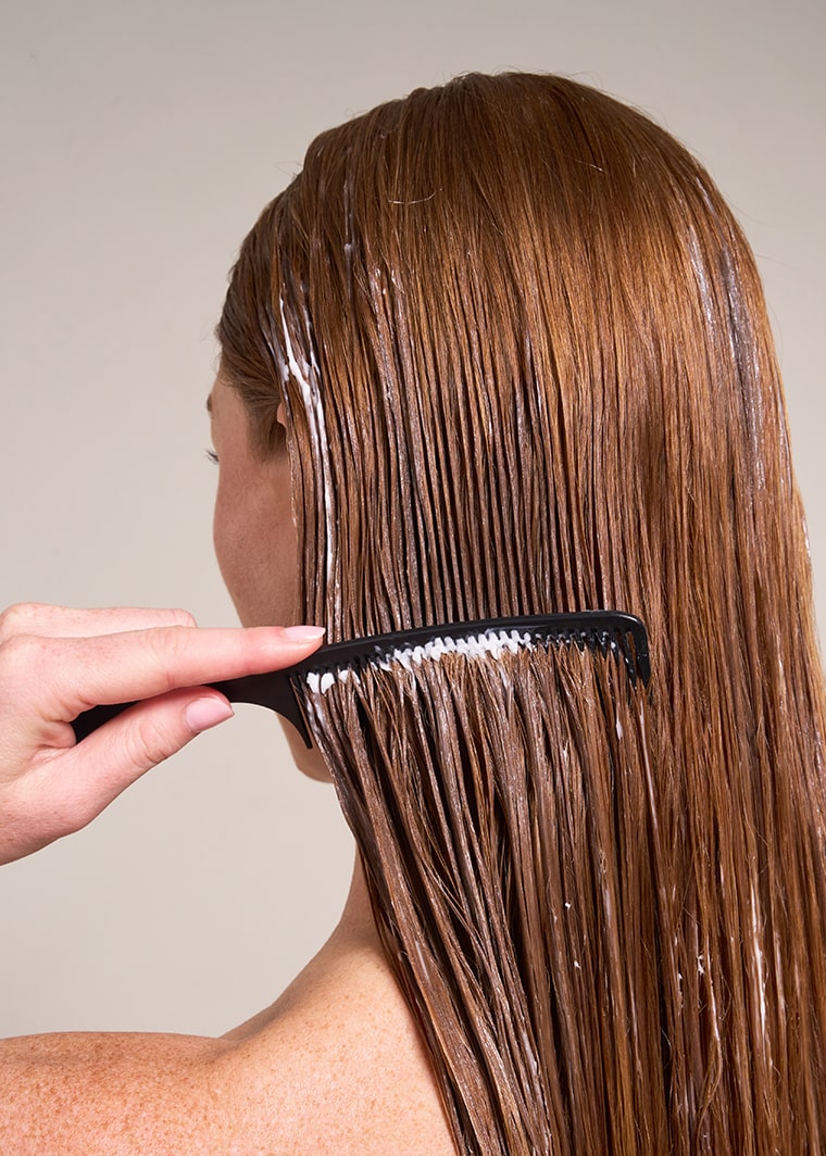 Close-up side view of a woman using a comb to detangle wet hair,