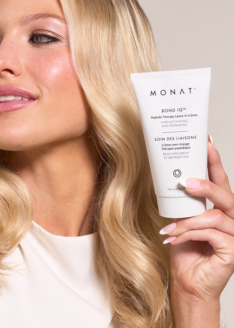 Close-up of a blonde woman with sleek hair holding the tube of crème near her face.