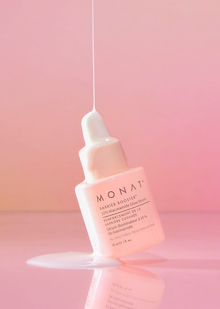 Close-up of MONAT Barrier Booster™ Niacinamide Glow Serum bottle on a light pink surface.