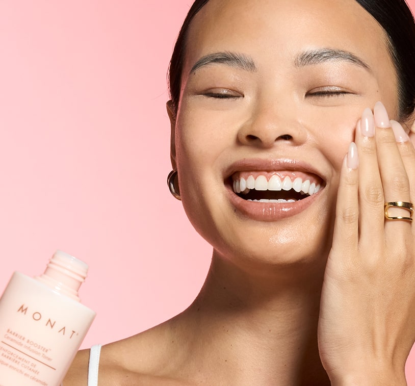 Woman in a white top smiling while gently applying the MONAT Barrier Booster™ Ceramide Infusion Toner to her face