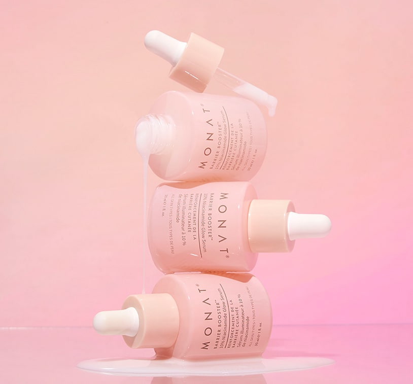 MONAT Barrier Booster™ Niacinamide Glow Serum bottles lying side by side on a pastel pink surface.