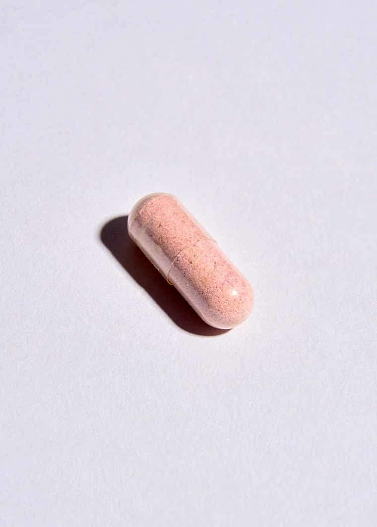 Single pink supplement capsule on light purple background