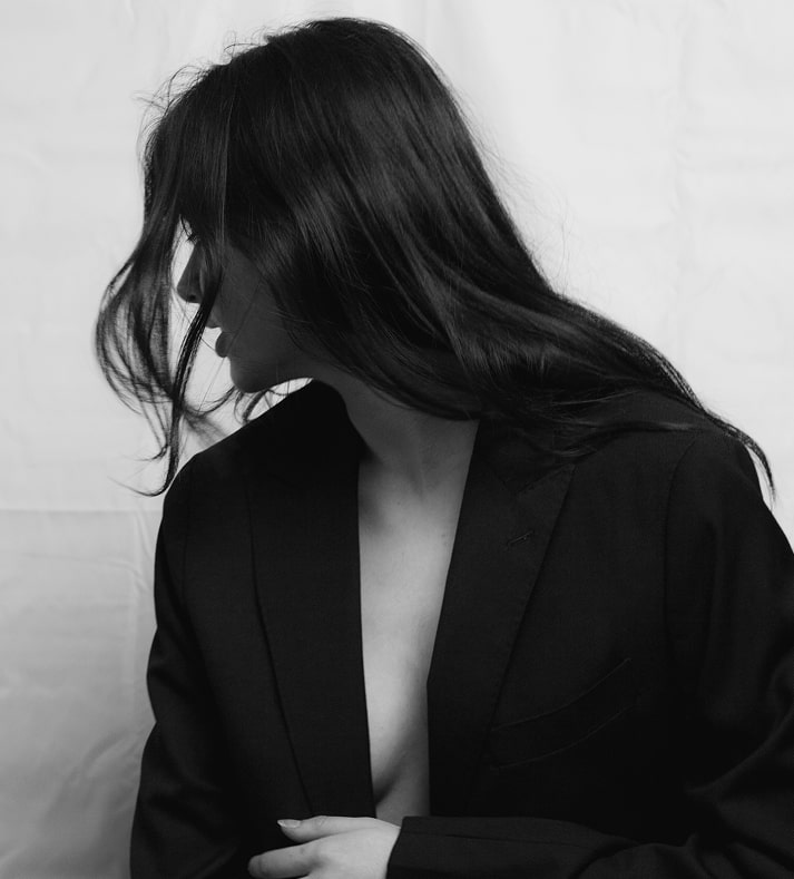 A moody black and white portrait of a person with long dark hair that partially obscures their face as they look downward