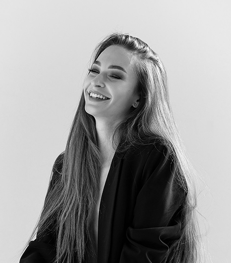 A black and white portrait of a young woman with long straight hair, smiling warmly while looking upward