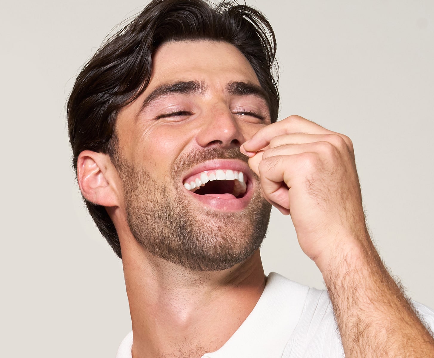 A man with dark hair and facial stubble laughs joyfully with his eyes closed, holding his hand a pill of MONAT IR supllement