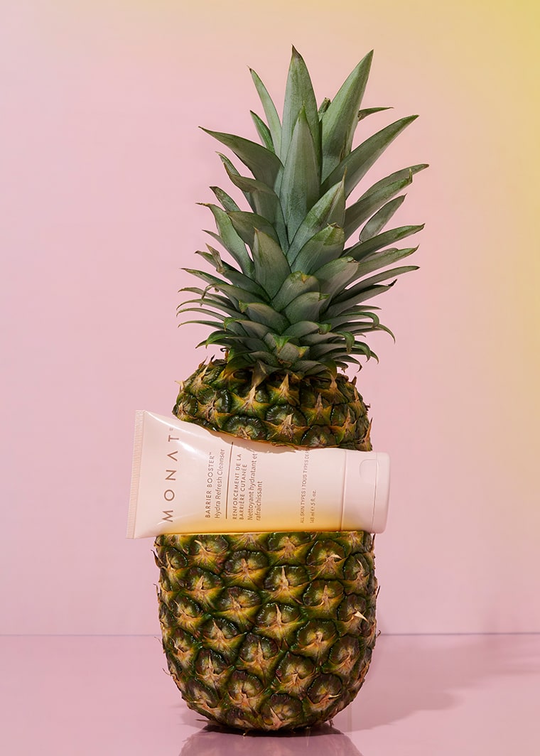 MONAT Barrier Booster Hydra Refresh Cleanser tube artistically placed in the middle of a sliced pineapple