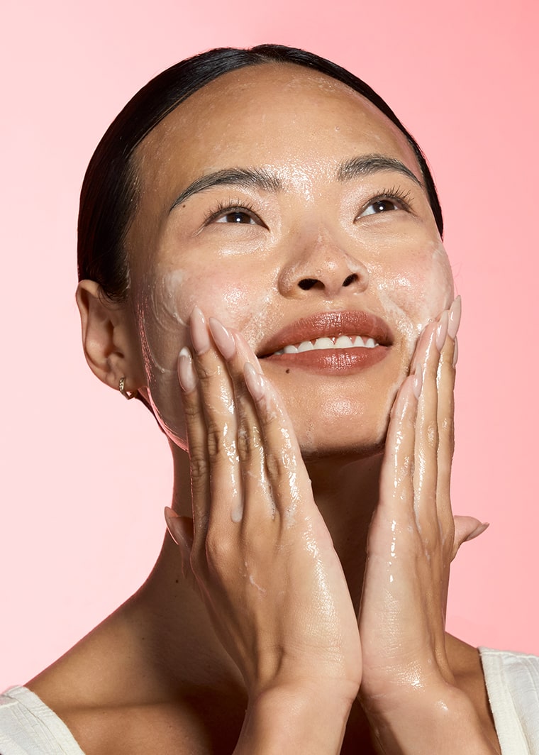woman with radiant skin applying cleanser to her face with both hands