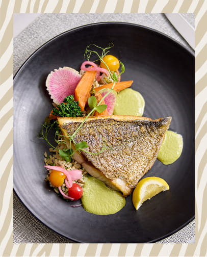 Gourmet Hawaiian dish featuring fresh fish with colorful vegetables and edible flowers on a dark plate