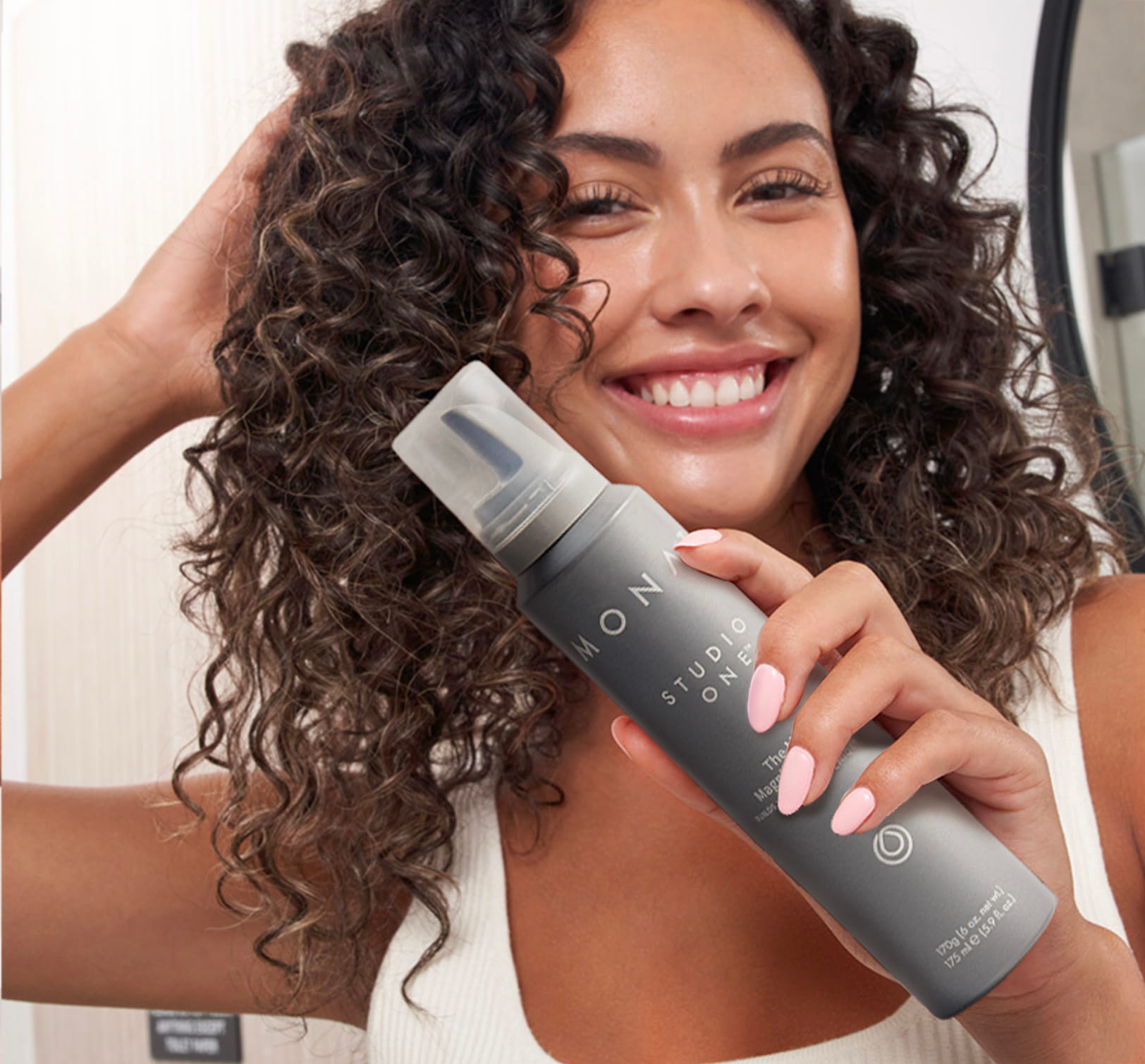 Brunette female with curls holding MONAT STUDIO ONE™ The Moxie™ Magnifying Mousse.
