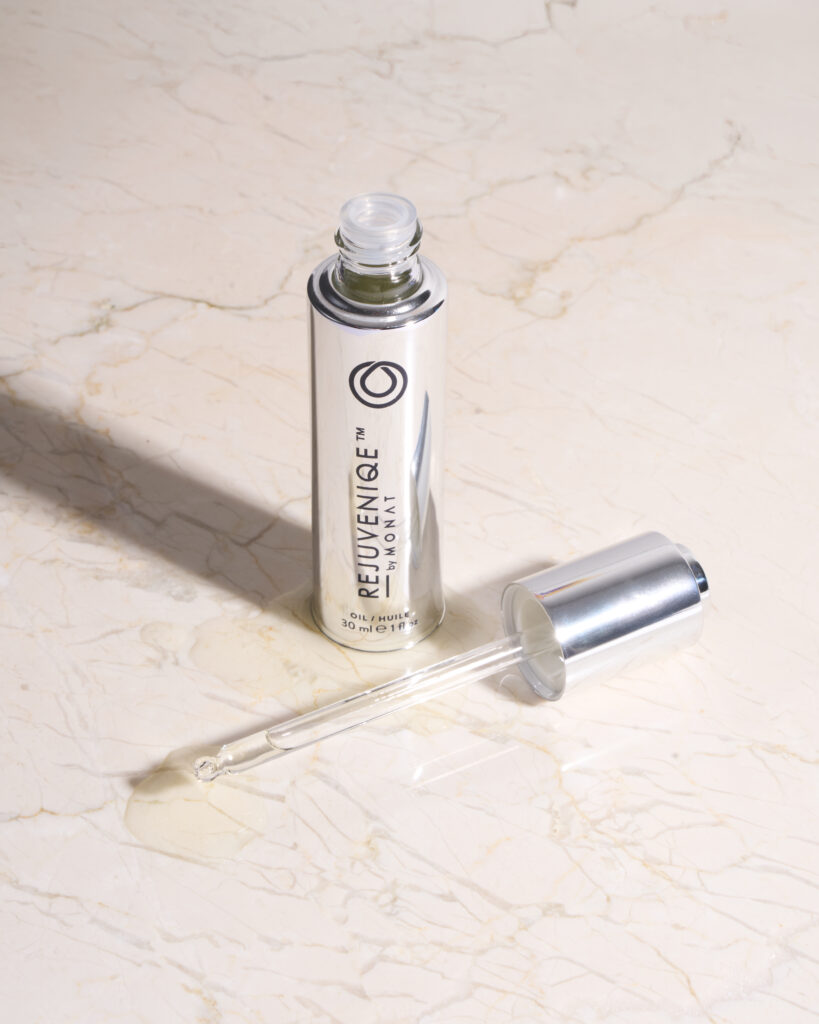 Close-up of a silver cylindrical cosmetic bottle with the dropper cap removed, on a pale marble surface.
