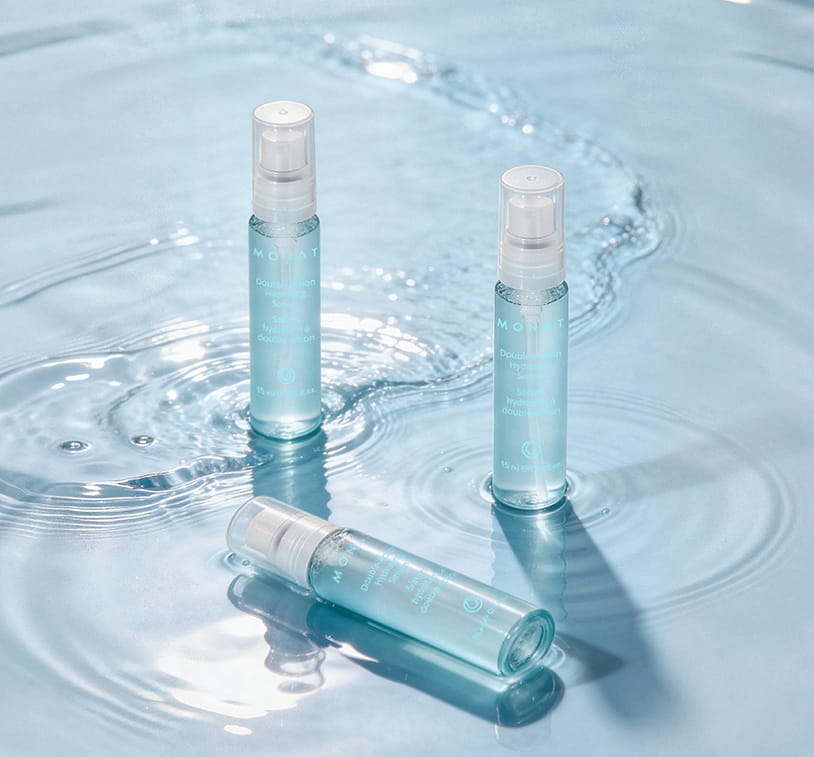 Three MONAT Double-Action Hydrating Serum vials arranged on a light blue water surface with gentle ripples — two standing upright and one lying flat — showcasing the set from multiple angles.