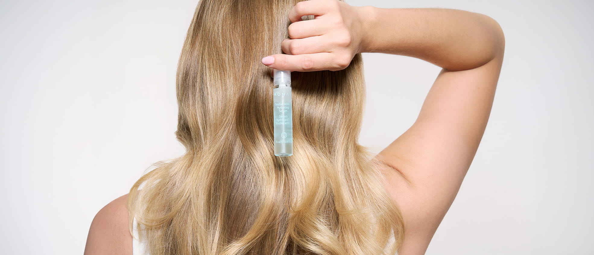 Close-up portrait of a woman with long, straight brown hair and brown eyes, holding a MONAT BOND IQ Fortifying Conditioner tube