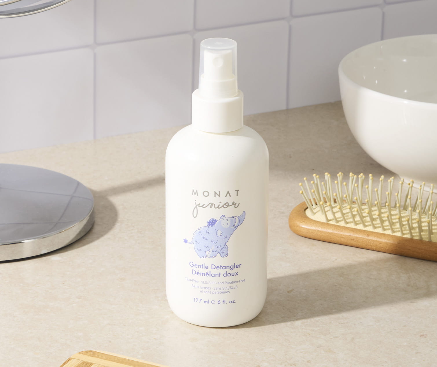  MONAT Junior Gentle Detangler spray bottle on a bathroom countertop beside a hairbrush and sink.
