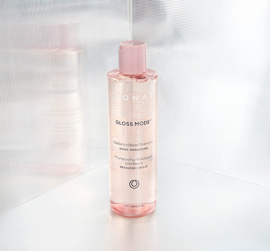 Pink-toned Gloss Mode Radiance Reset Shampoo bottle standing on a bright, reflective surface against a softly textured translucent background.
