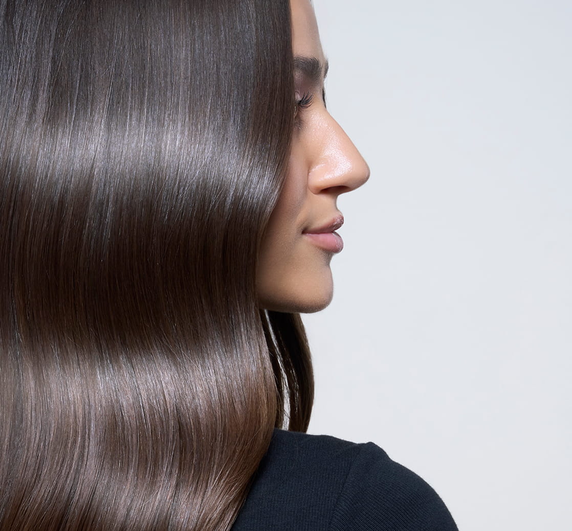 Side-profile close-up of a woman with long, smooth, glossy brown hair, emphasizing the hair’s shine and sleek texture.