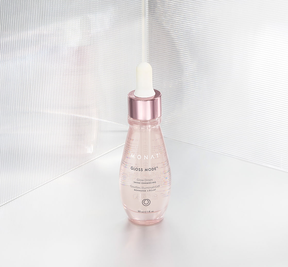 Pink-toned Gloss Mode Glow Drops bottle with a dropper cap displayed against a bright, textured white background.