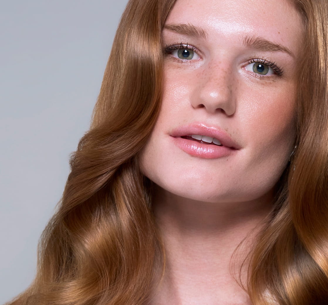 Close-up portrait of a woman with long, glossy, softly waved red hair.