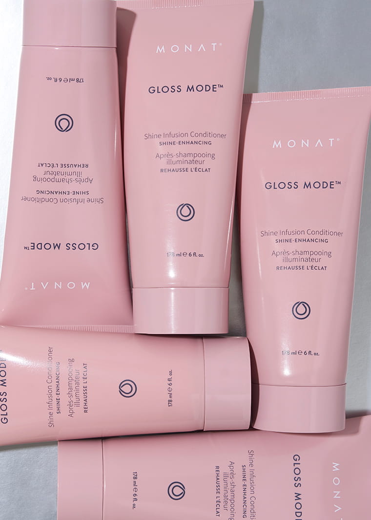 Several pink MONAT GLOSS MODE Shine Infusion Conditioner tubes arranged against a pale gray surface, showcasing the product packaging