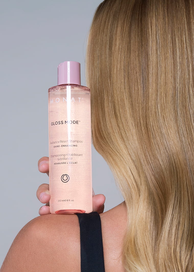 MONAT Gloss Mode shampoo bottle held in front of long, smooth blonde hair