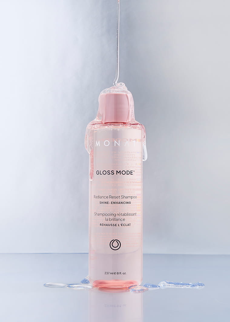 MONAT Gloss Mode Radiance Reset Shampoo bottle standing on a reflective surface with water dripping over the bottle.