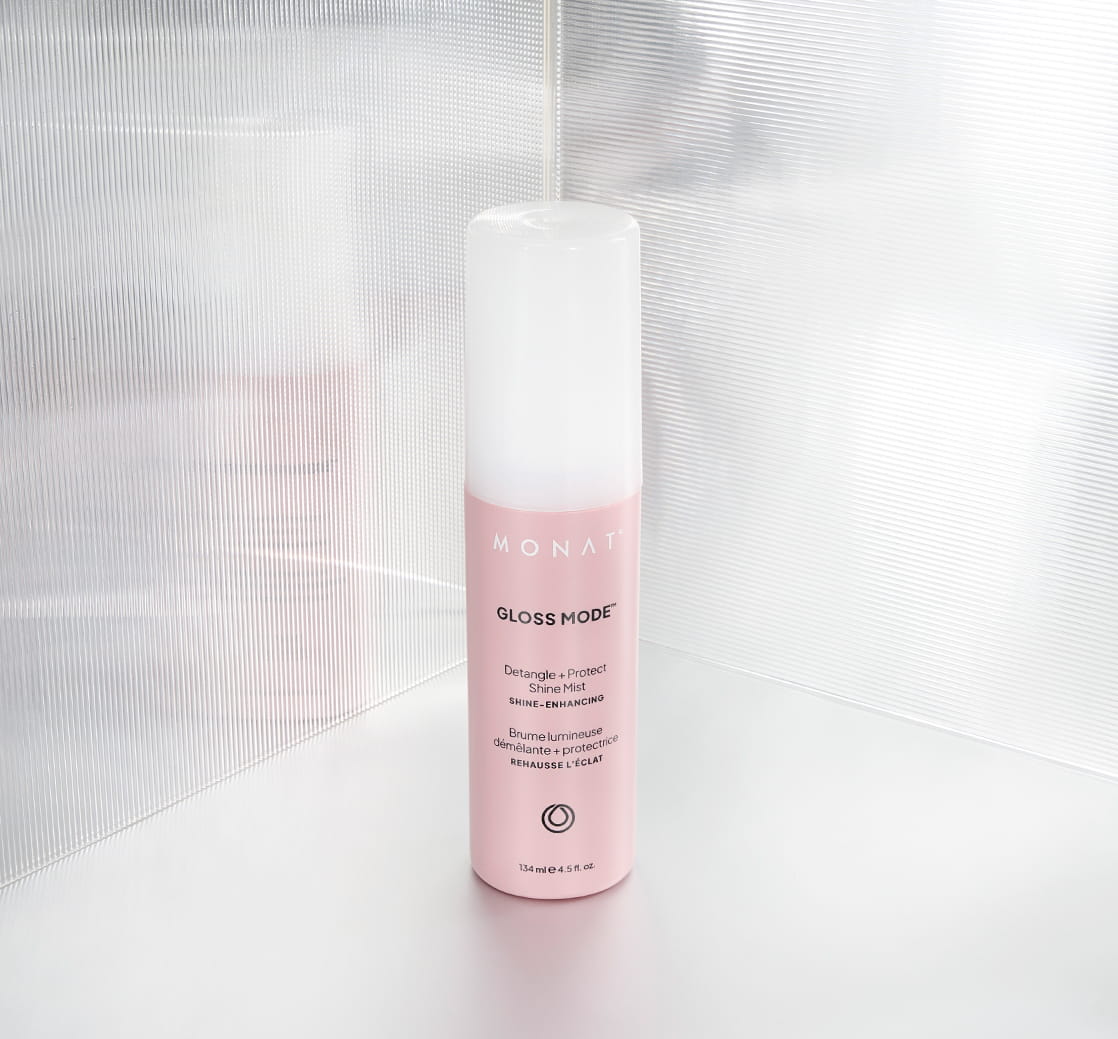 Pink MONAT Gloss Mode bottle of Detangle + Protect Shine Mist standing upright against a bright, translucent textured backdrop