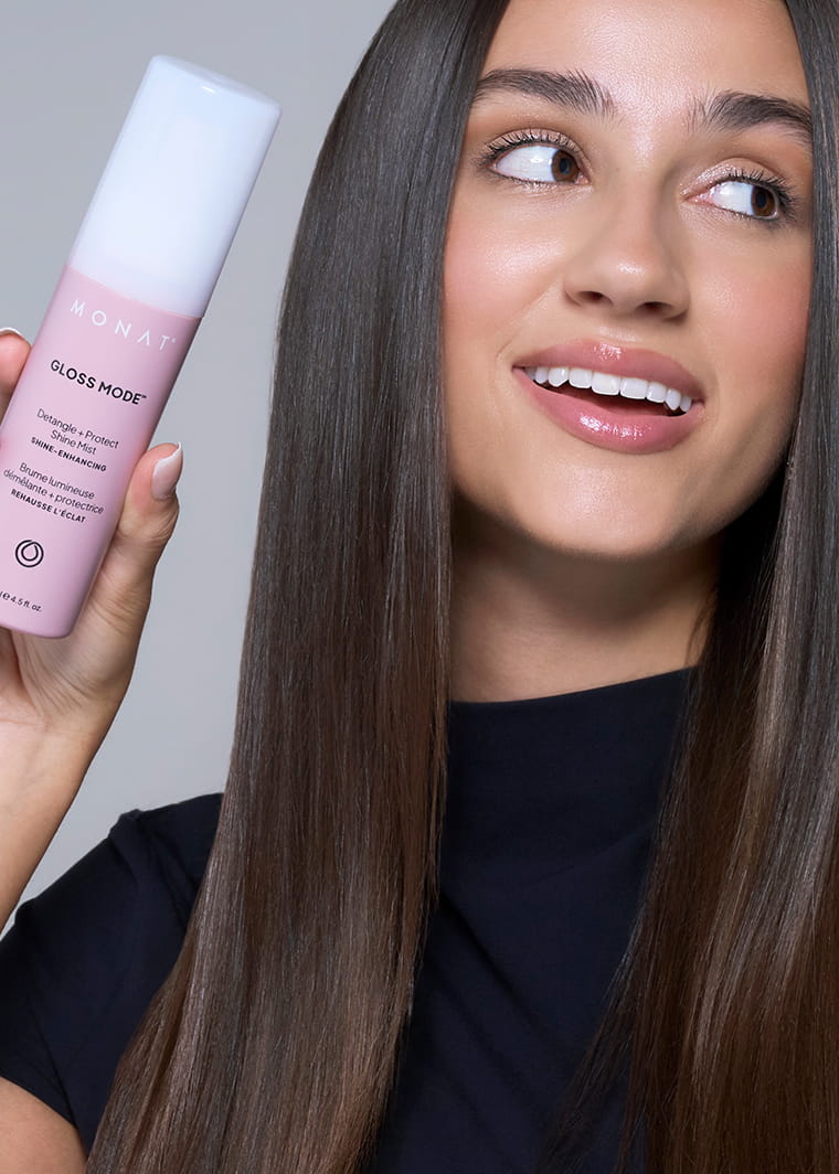 MONAT Gloss Mode bottle held beside a woman with long, straight brown hair