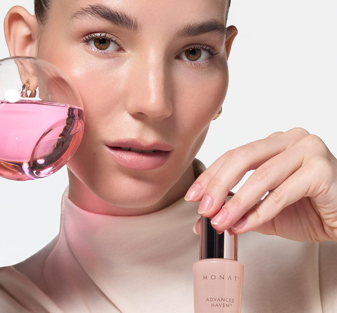 Woman holding MONAT ADVANCED HAVEN™ Longevity Serum near her face, framed by pink crystals