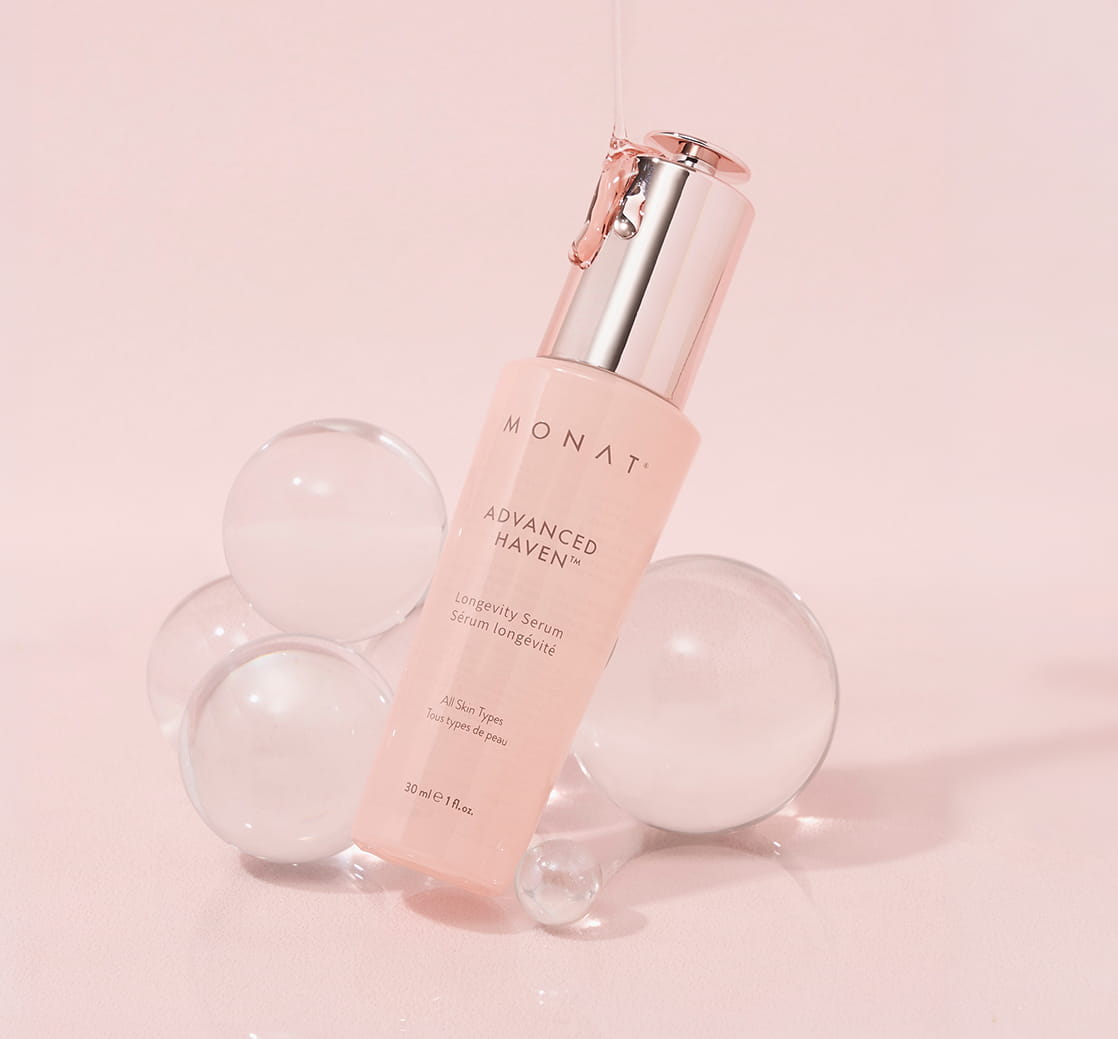 MONAT ADVANCED HAVEN™ Longevity Serum bottle resting on clear glass spheres against a pink background