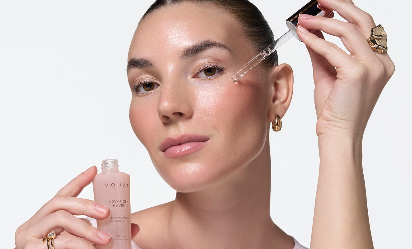 Woman applying MONAT ADVANCED HAVEN™ Longevity Serum to her face with a dropper while holding the bottle