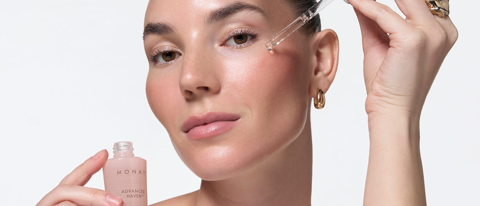 Woman applying MONAT ADVANCED HAVEN™ Longevity Serum to her face with a dropper while holding the bottle