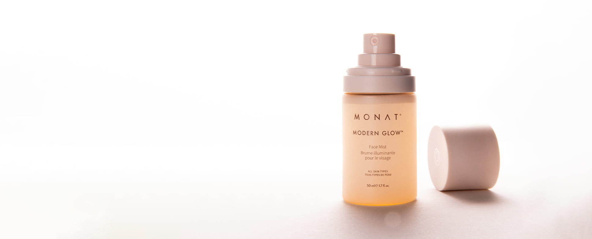 MONAT Modern Glow Face Mist bottle with its cap beside it on a soft pink background.